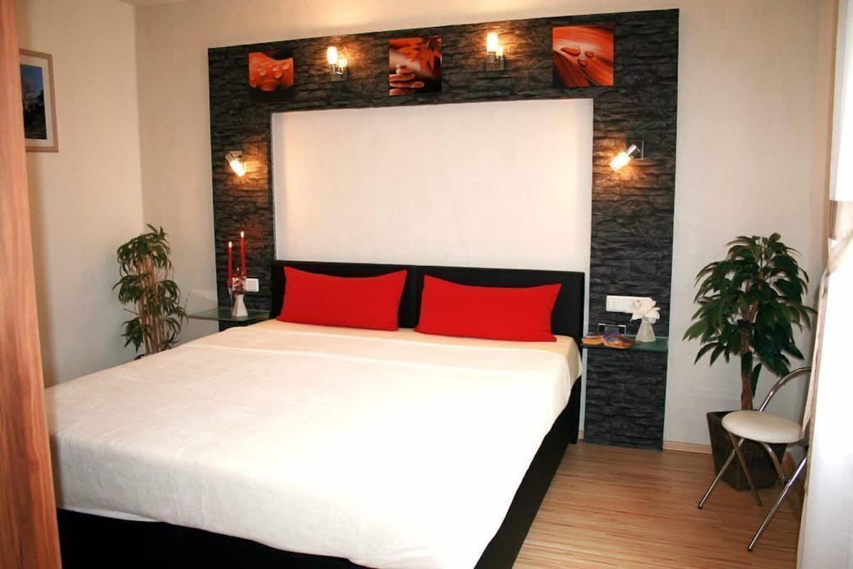 A modern bedroom with a large bed, red and black pillows, a stone accent wall, and wall-mounted lights.