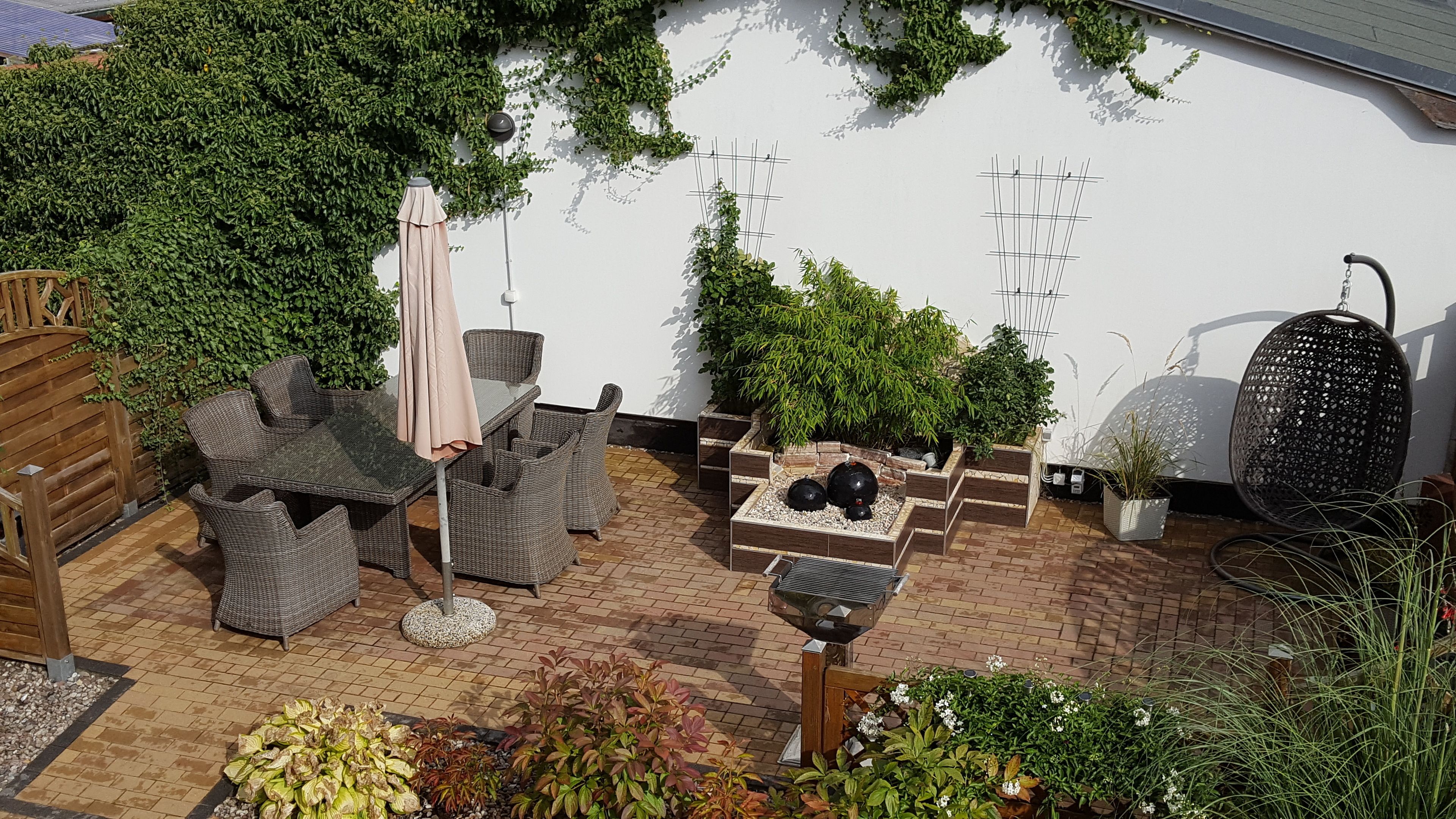 Une terrasse dotée de meubles en osier, d’un fauteuil suspendu et de plantes en pot.