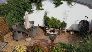 Une terrasse dotée de meubles en osier, d’un fauteuil suspendu et de plantes en pot.