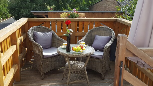 A wooden deck with wicker chairs and a small table, featuring a fruit bowl and a vase with flowers. - Ferienwohnungen Villa Waldblick (Zempin)
