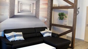 A modern room with a black sofa, a white table, and a wooden partition with a plant. - Ferienwohnungen Villa Waldblick (Zempin)