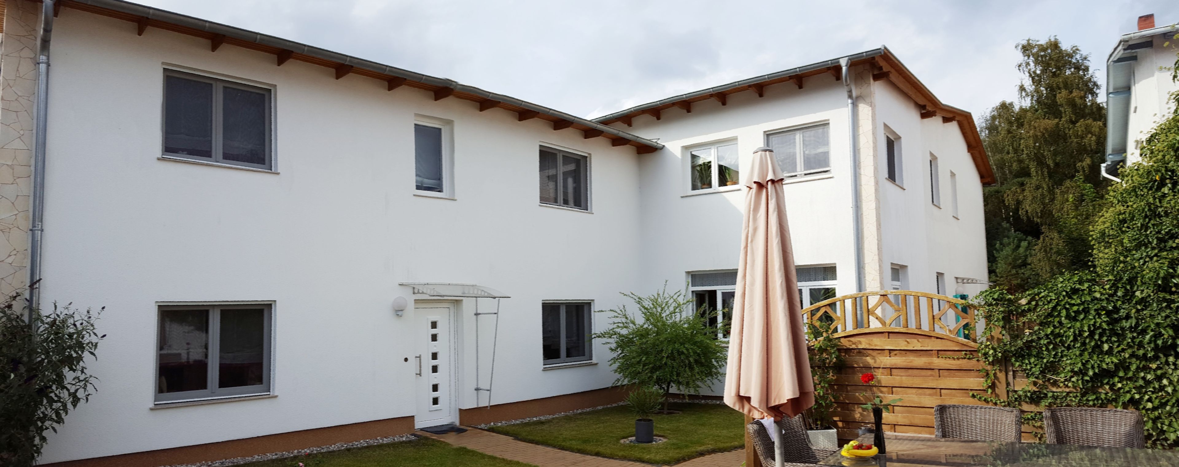 A two-story building with multiple windows, a wooden door, and a small garden area with a table and chairs.