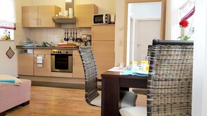 A compact kitchen with wooden cabinets, a microwave, and a dining area with wicker chairs. - Ferienwohnungen Villa Waldblick (Zempin)