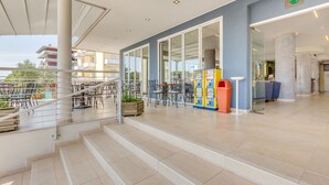 A modern indoor area with a staircase leading to an upper level, featuring outdoor seating and a vending machine. - Hotel Ambassador (Caorle)