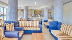 A hotel lobby with multiple sofas and armchairs, a reception desk, and large columns. - Hotel Ambassador (Caorle)