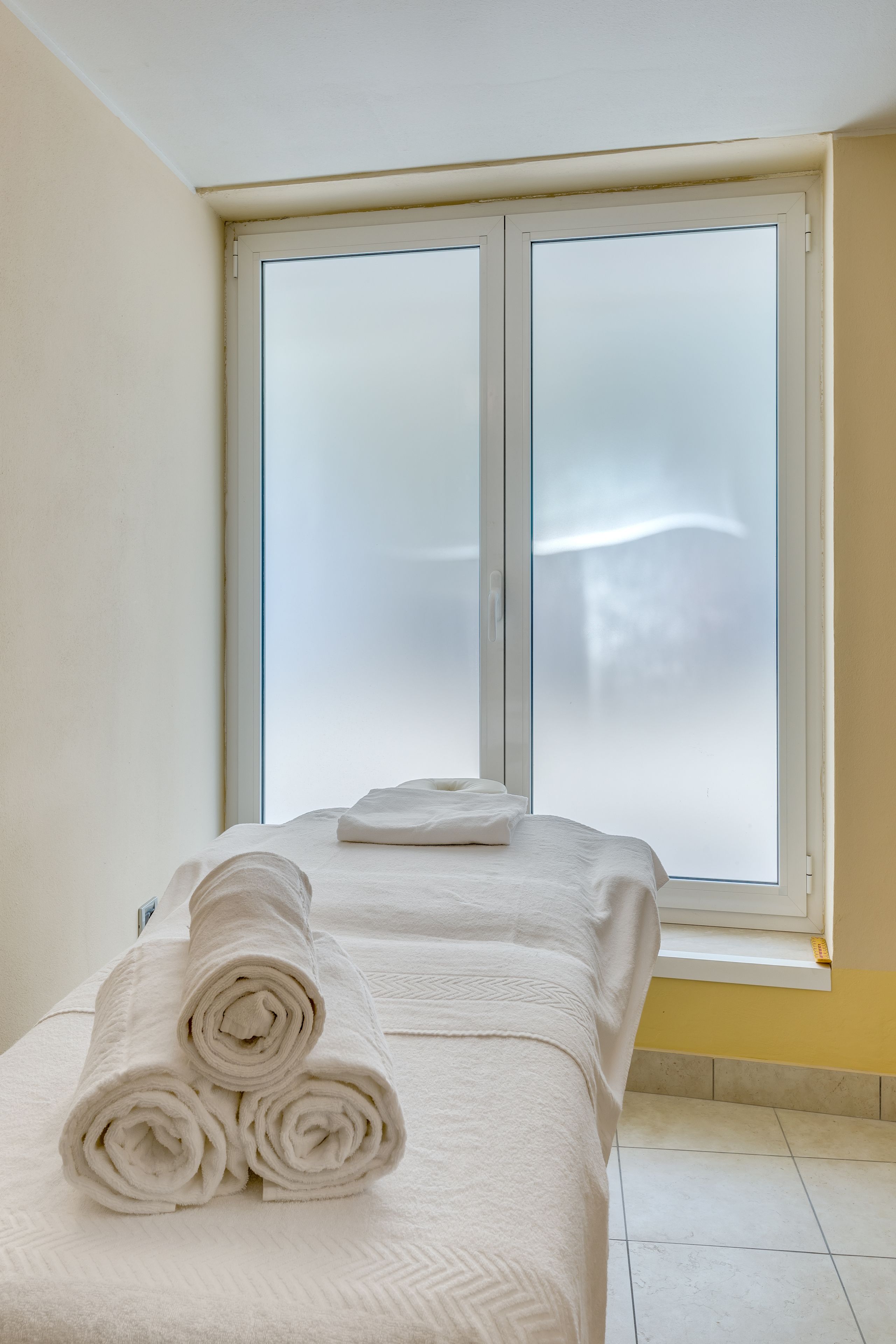 A hotel room with a bed, a window with frosted glass, and a towel on the bed.