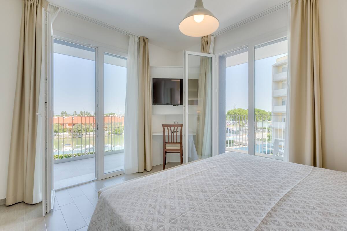 Una habitación de hotel con una cama grande, un televisor montado en la pared y un balcón con vista a la ciudad.