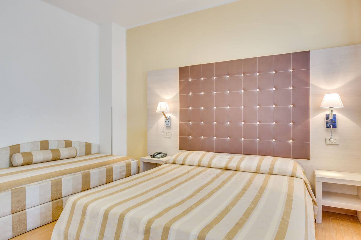 Habitación de hotel con una cama grande, una cama más pequeña, una mesita de noche con lámpara y un teléfono en el buró.