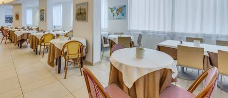 A dining area with round tables and chairs, a map on the wall, and a view of the city through large windows.
