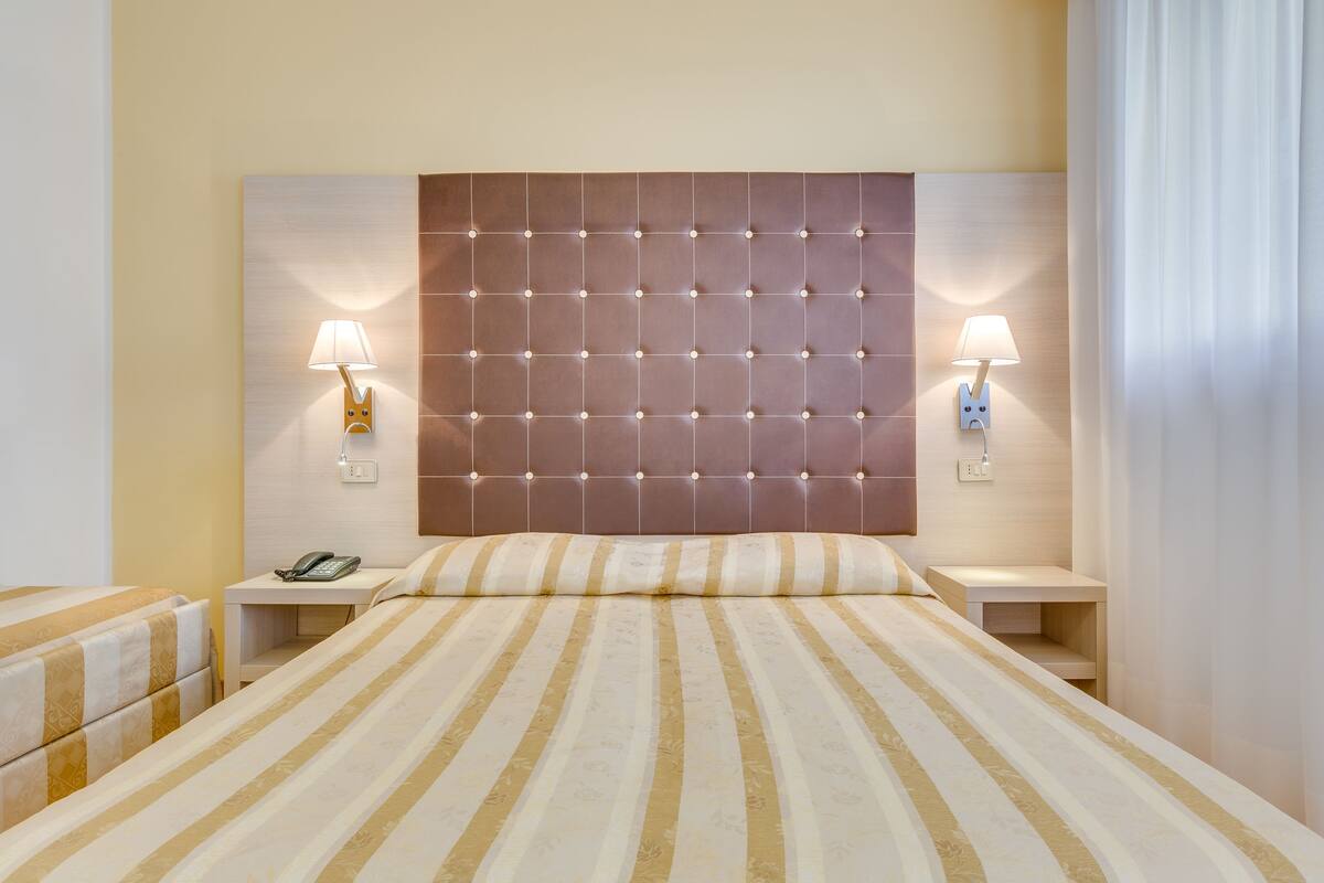 Una habitación de hotel con una cama grande, dos mesitas de noche, un teléfono y dos lámparas de pared.