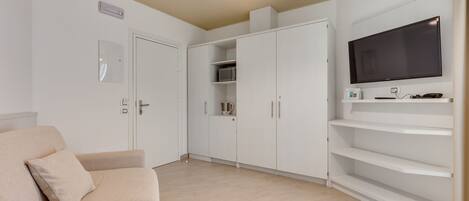 A modern living room with a beige sofa, white cabinets, a flat-screen TV, and a ceiling light.