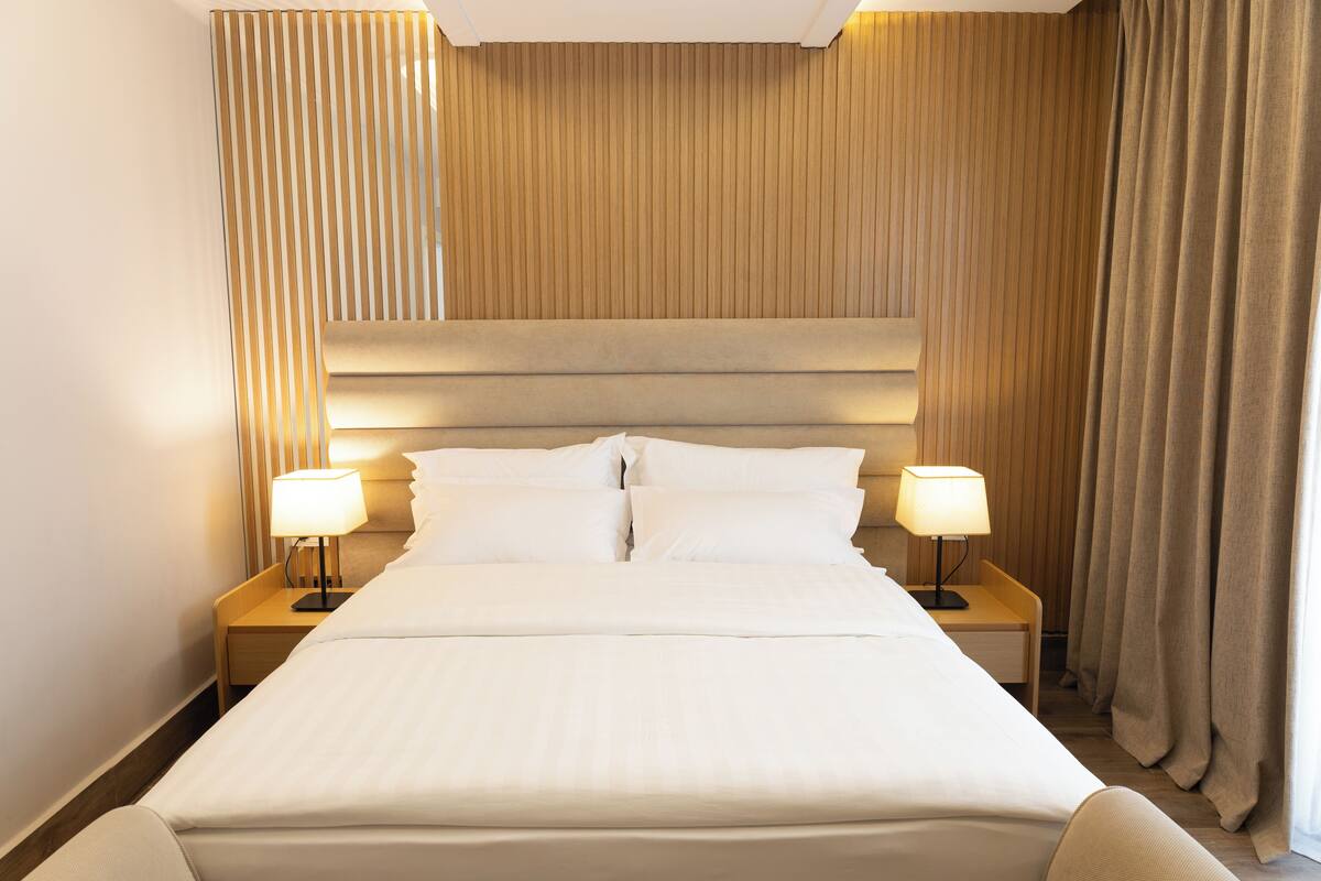 A neatly made bed with white linens, two bedside tables with lamps, and a wooden headboard.