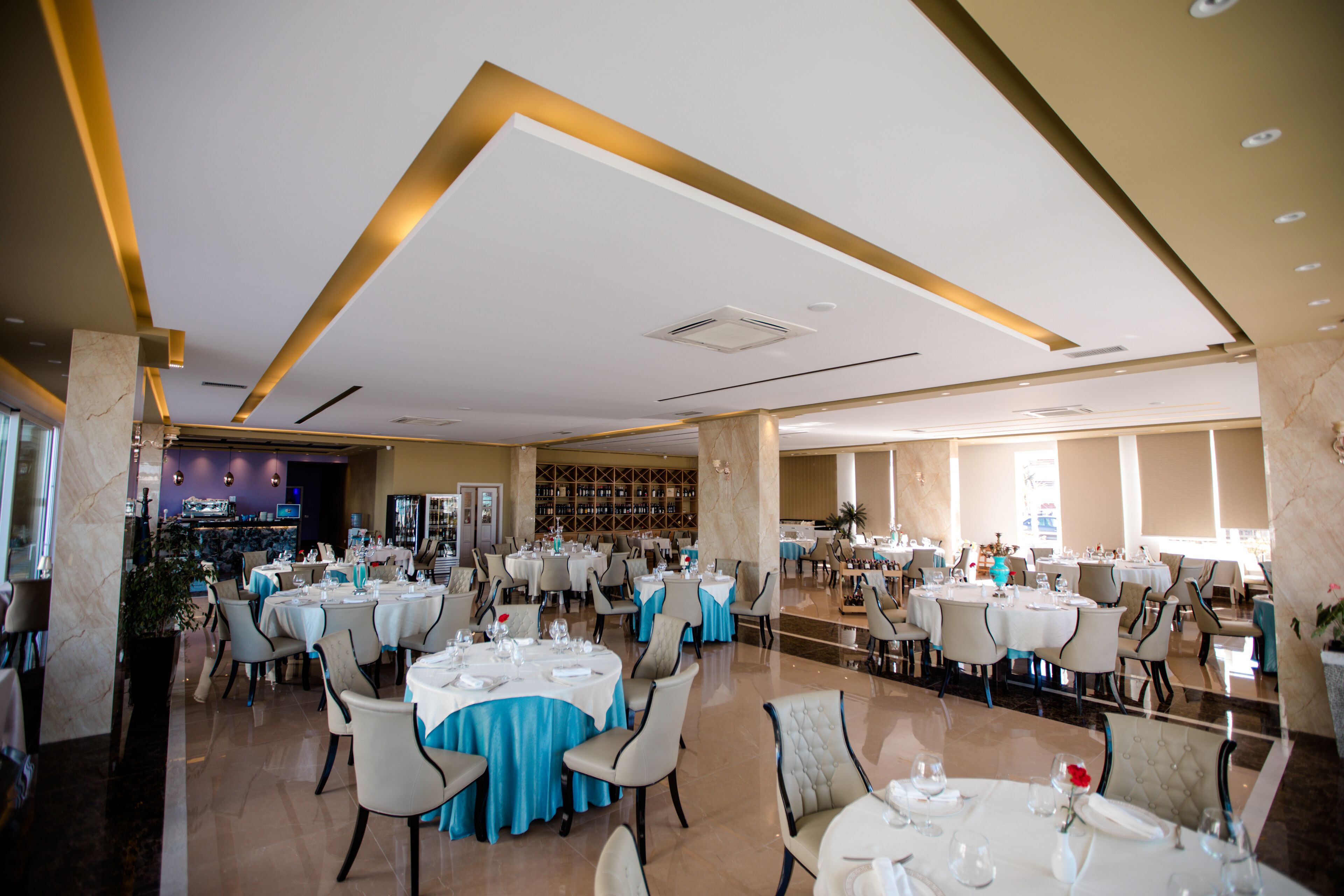 A spacious dining area with multiple round tables, each set with white tablecloths and blue napkins.