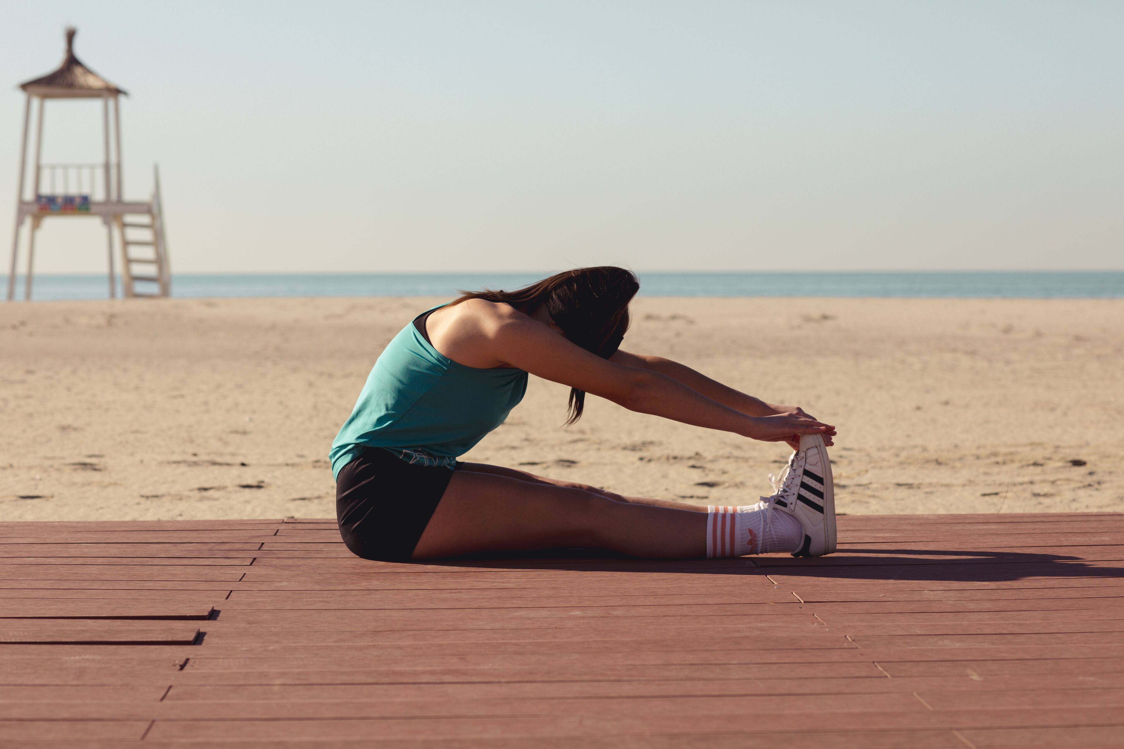 A person stretching on a wooden deck at a beach with a lifeguard tower in the background.