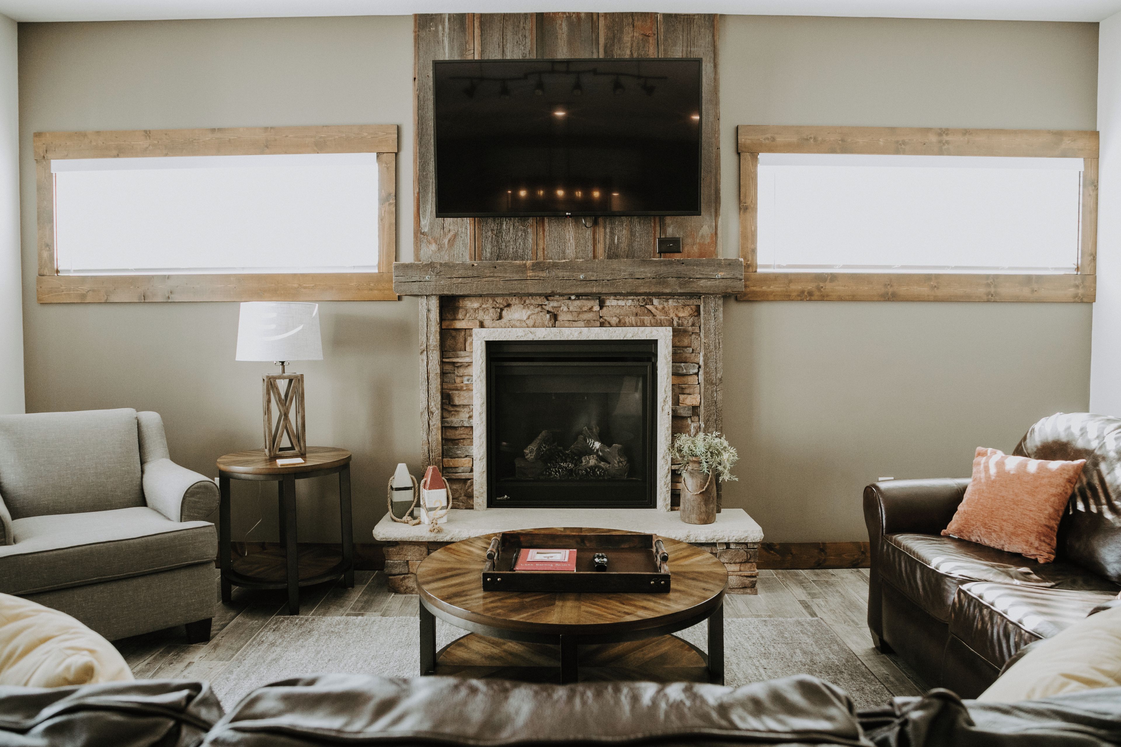 A living room with a stone fireplace, a flat-screen TV mounted above it, and a large window on one side.