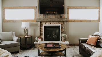 A living room with a stone fireplace, a flat-screen TV mounted above it, and a large window on one side.