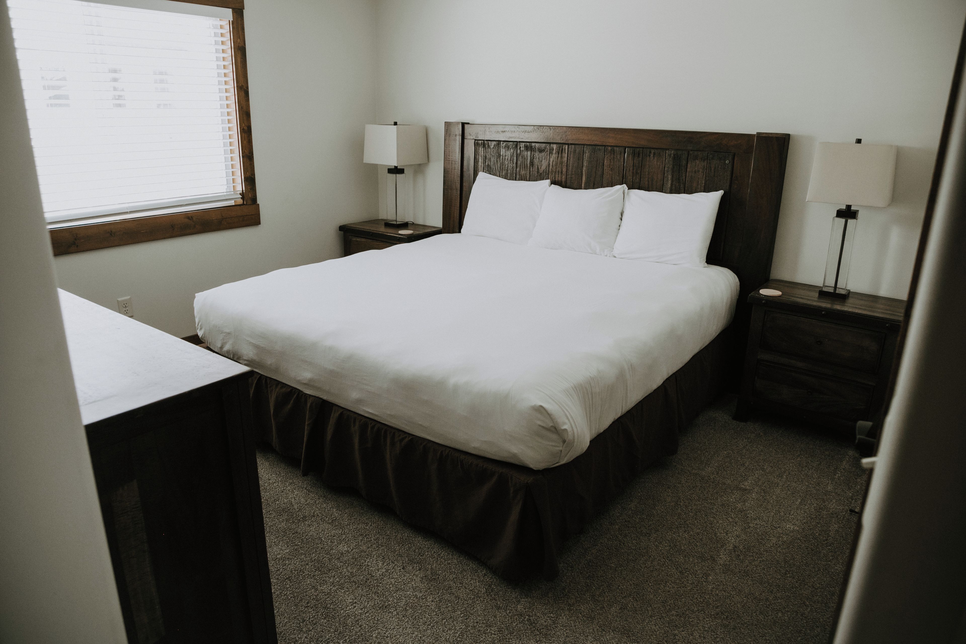 Une chambre d’hôtel avec un lit, des tables de chevet, un bureau et une fenêtre avec des stores.