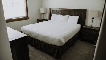 A hotel room with a bed, bedside tables, a desk, and a window with blinds.