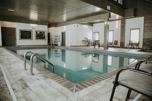 Une piscine dotée d’une terrasse carrelée, entourée d’un espace de détente avec des fauteuils et une table.