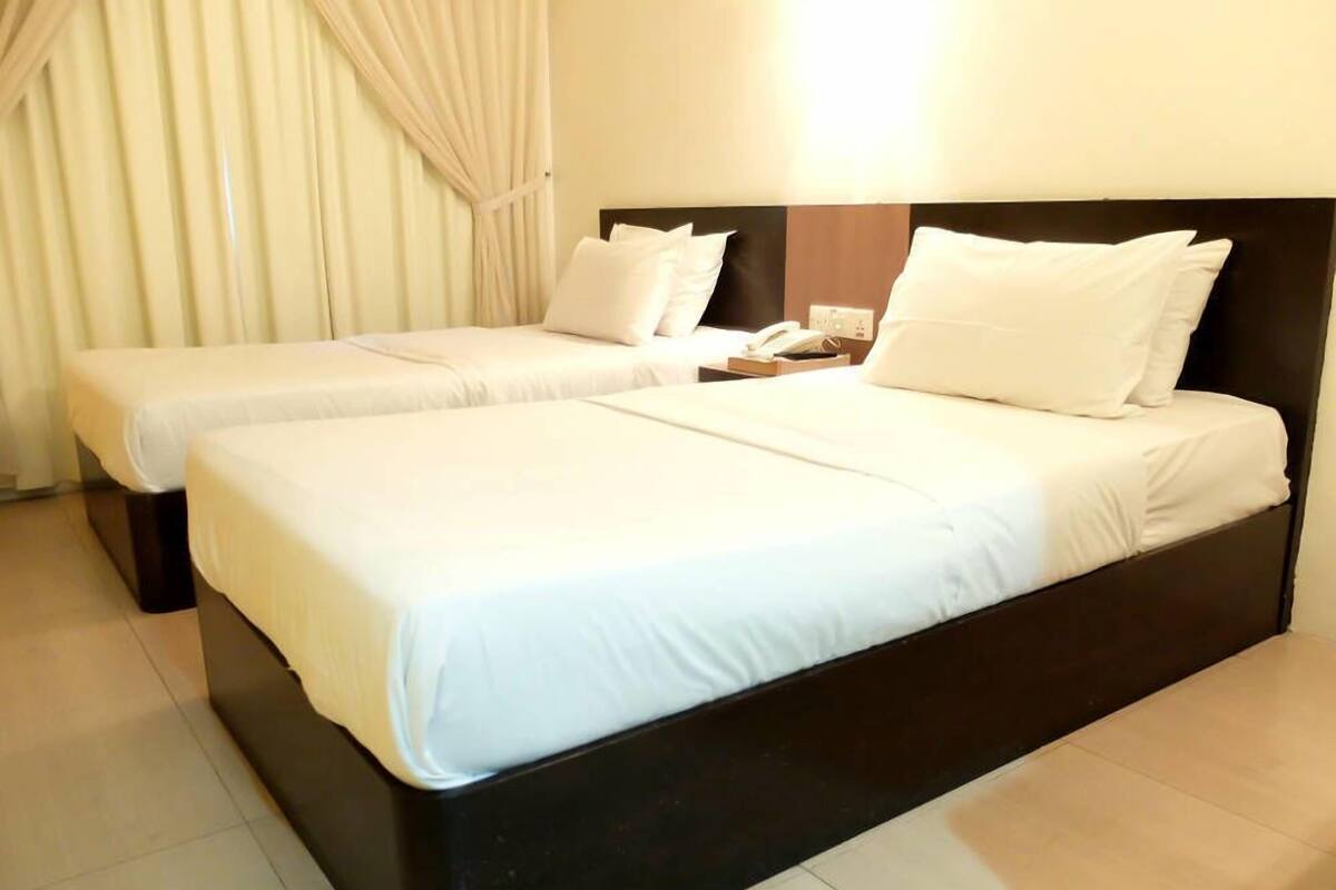A hotel room with two single beds, a nightstand with a telephone, and a window with curtains.