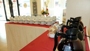 A table with multiple white cups and saucers, a coffee pot, and a teapot on a red tablecloth. - Streetview Hotel (Muar)