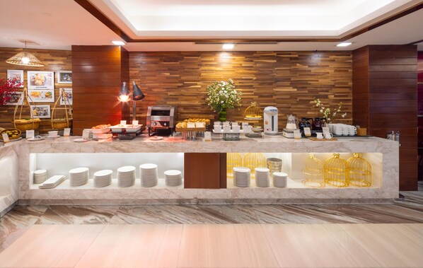 A hotel reception area with a marble counter, buffet with various food items, a coffee station, and a flower arrangement. - Winsuites Sai Gon Hotel (Ho Chi Minh City)