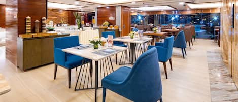 A modern restaurant with blue chairs, wooden tables, and a wooden reception desk.