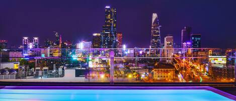 A nighttime cityscape with illuminated buildings and a pool area.