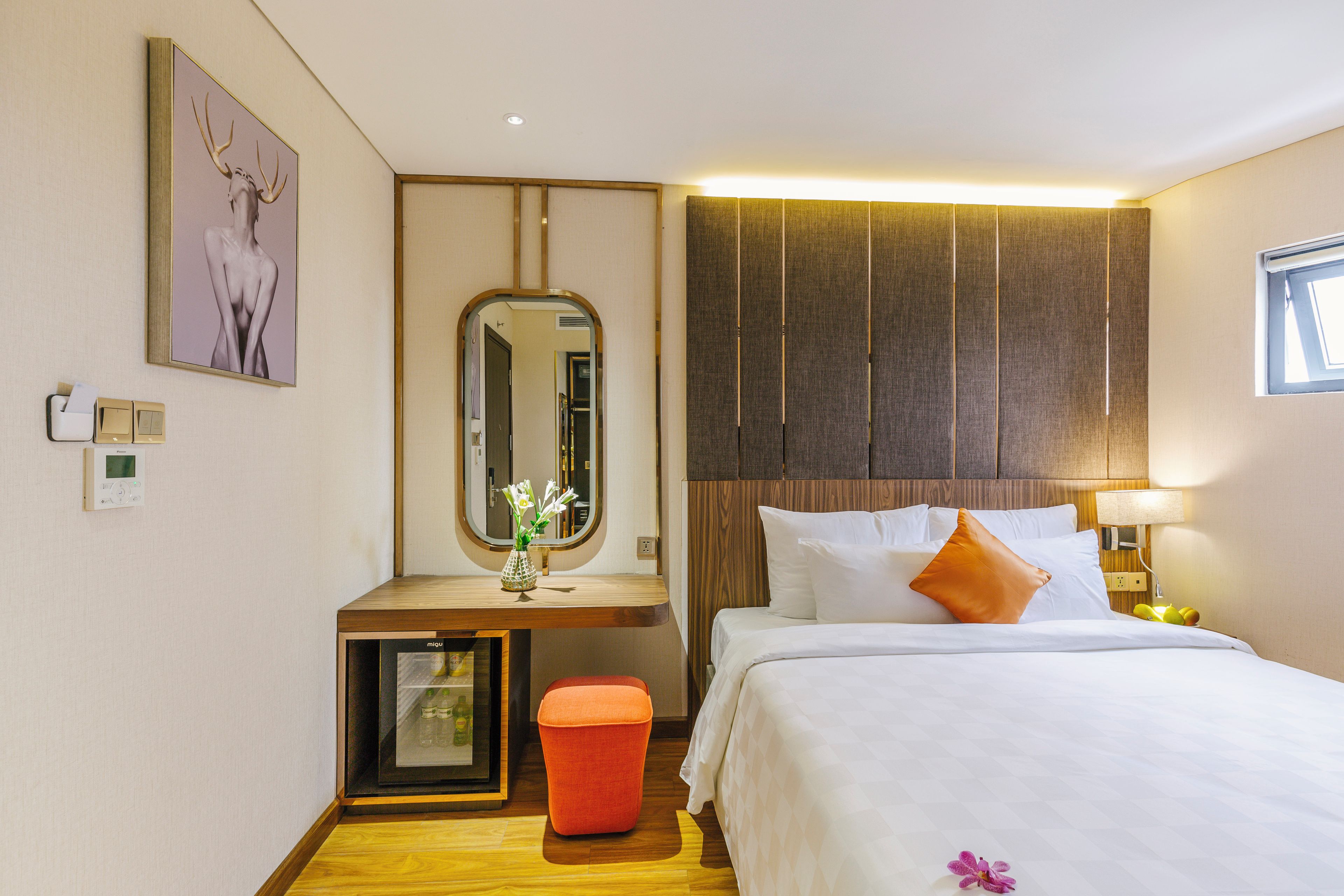 A hotel room with a bed, bedside table, mirror, and a small stool.