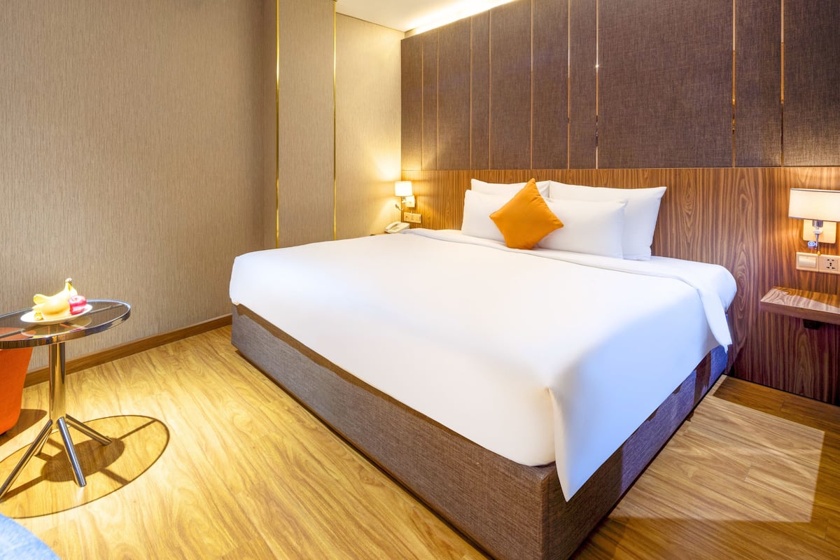 A hotel room with a large bed, a bedside table with a lamp, and a small round table with a chair.