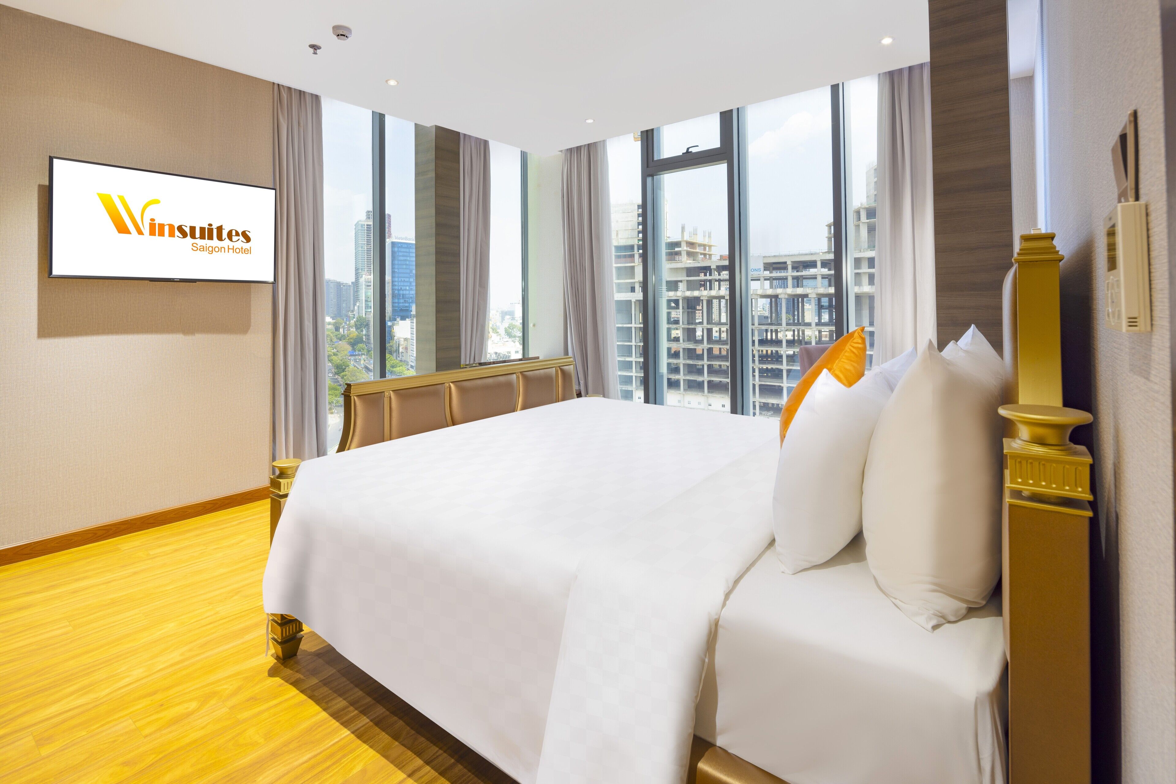 A hotel room with a large bed, a television mounted on the wall, and a view of the city through the windows.