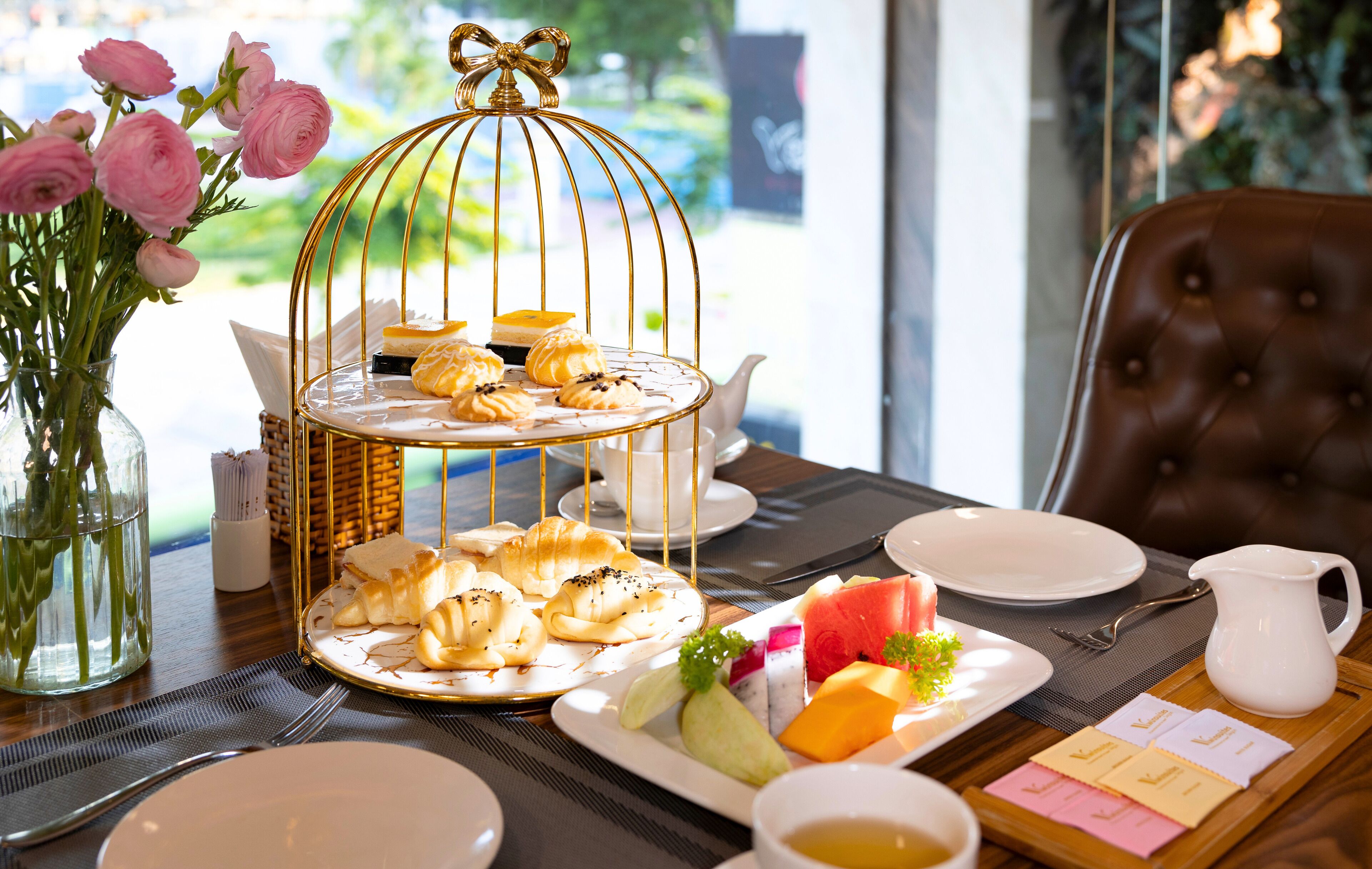 A table set with a tiered dessert stand, plates of food, a pitcher, and a vase with flowers.