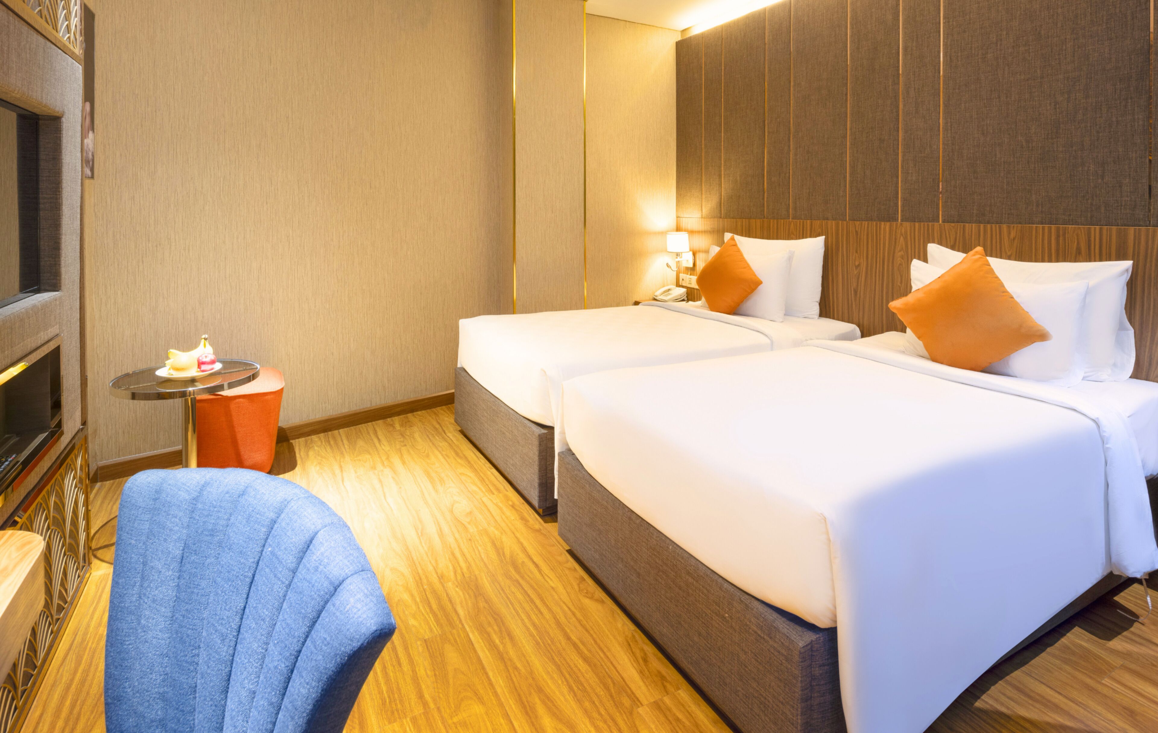 Een hotelkamer met twee bedden, een tafeltje met een lamp, een stoel en een televisie.