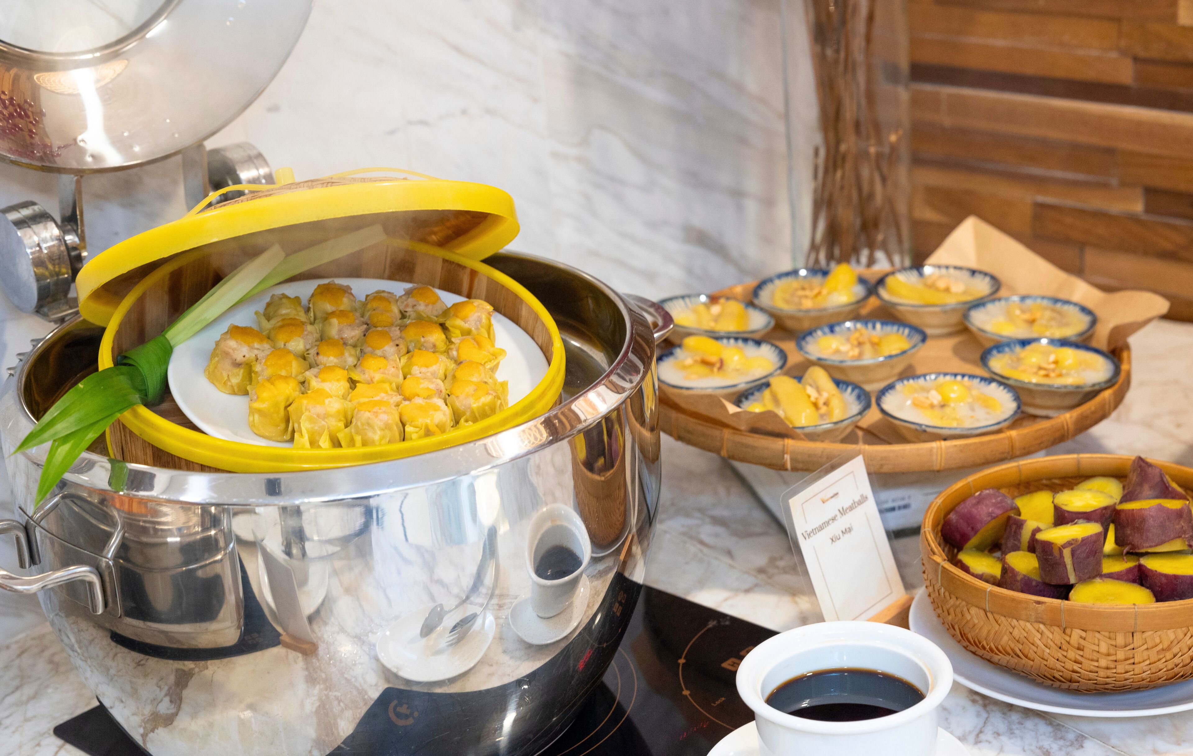Montaje tipo buffet con un recipiente de dumplings, tazones de rodajas de boniato y un cartel que indica cocina vietnamita.