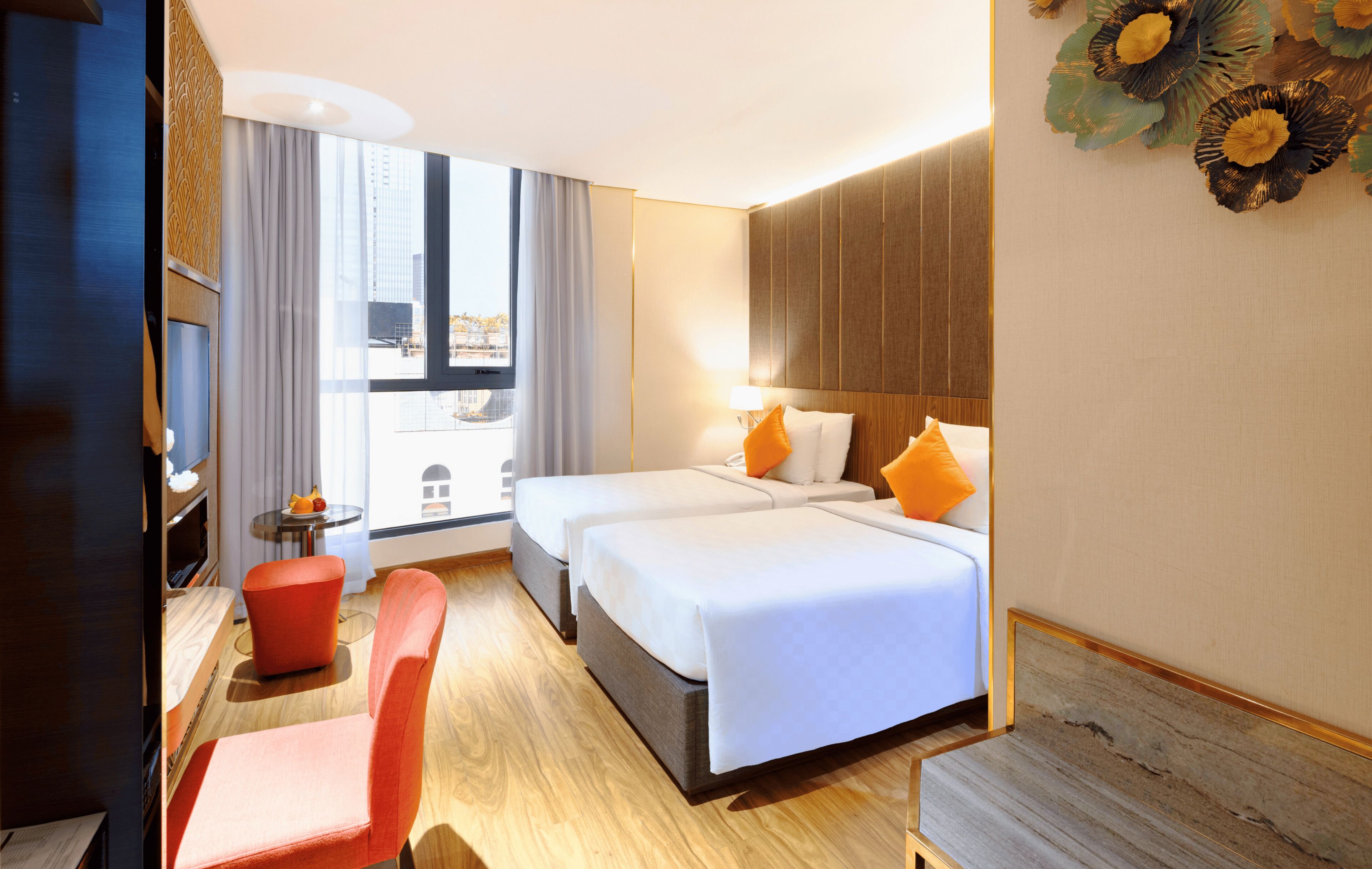 Une chambre d’hôtel avec deux lits, un bureau, une chaise et une grande fenêtre donnant sur des immeubles.
