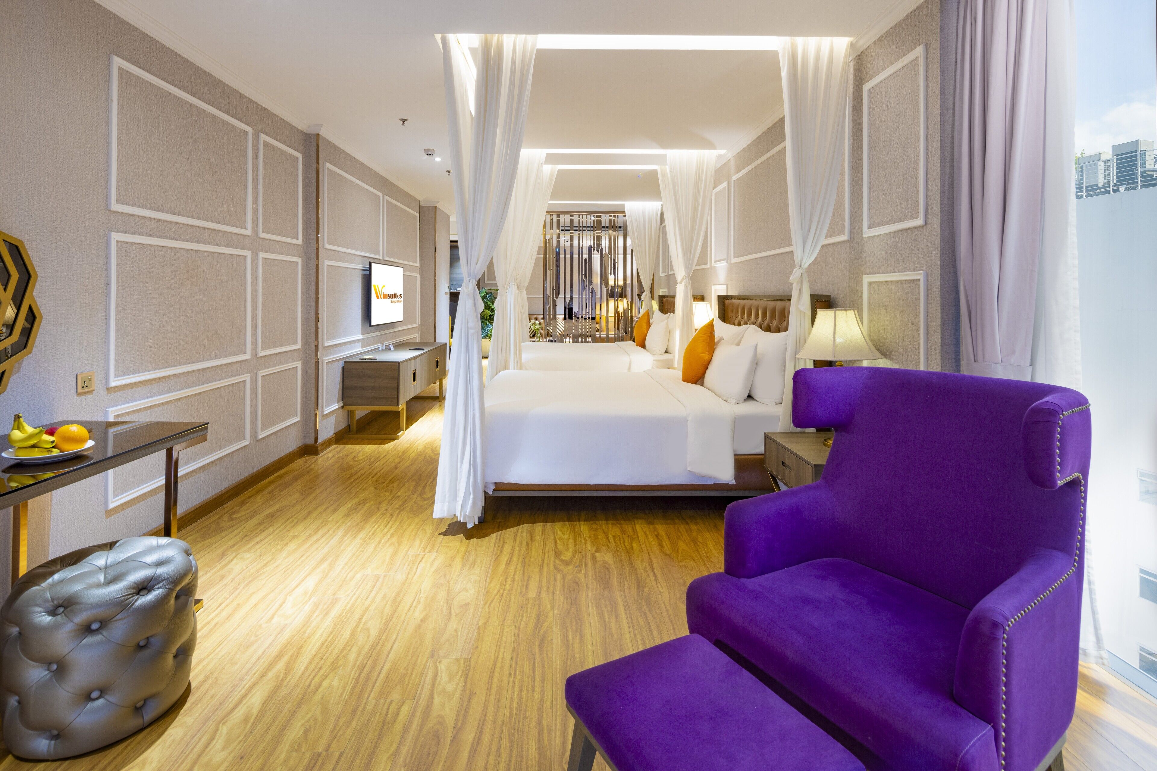 Een hotelkamer met een bed, een paarse fauteuil, een klein tafeltje met fruit en een televisie.