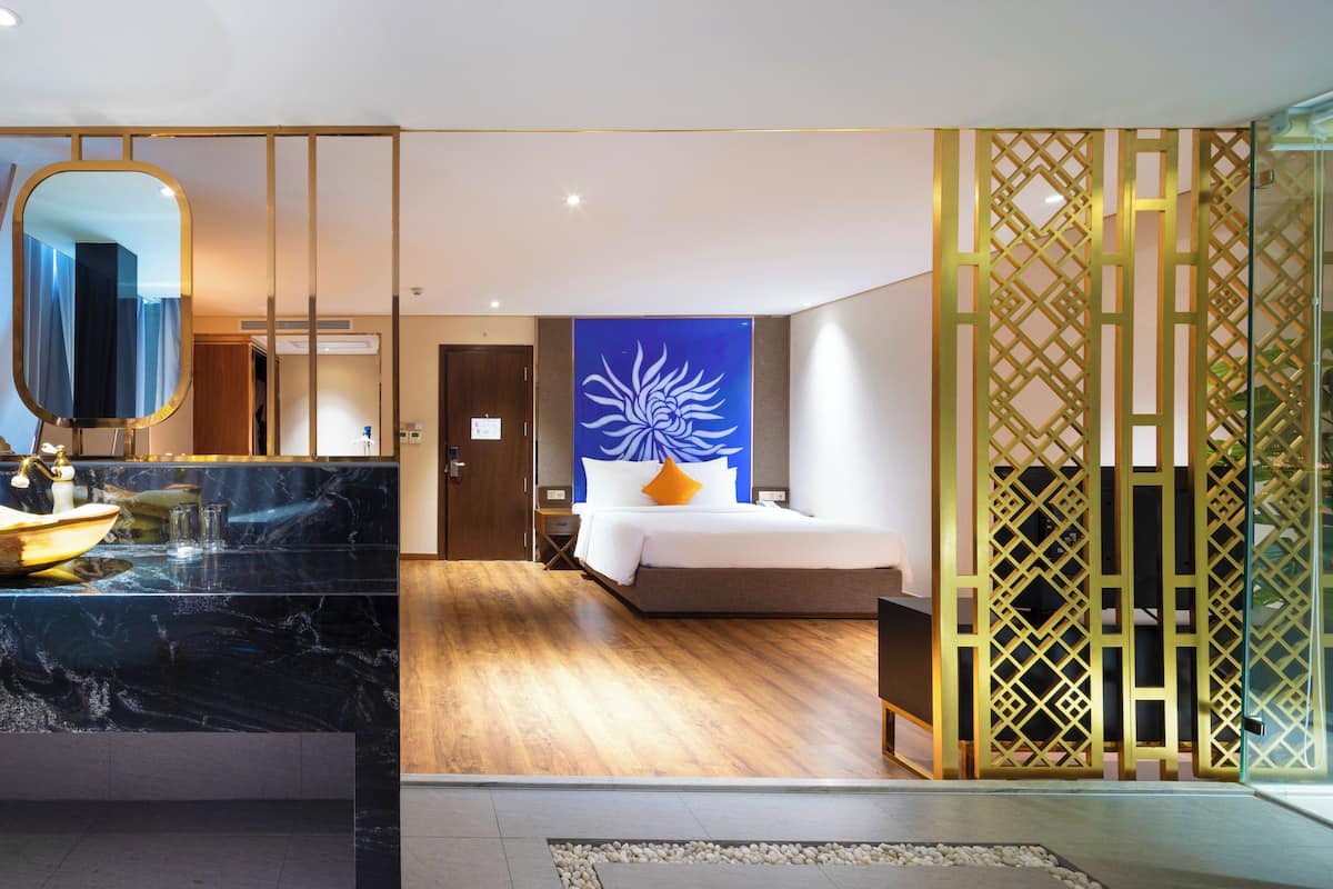A modern hotel room with a marble bathroom vanity, a large mirror, a bed with a blue floral wall art, and a wooden floor.