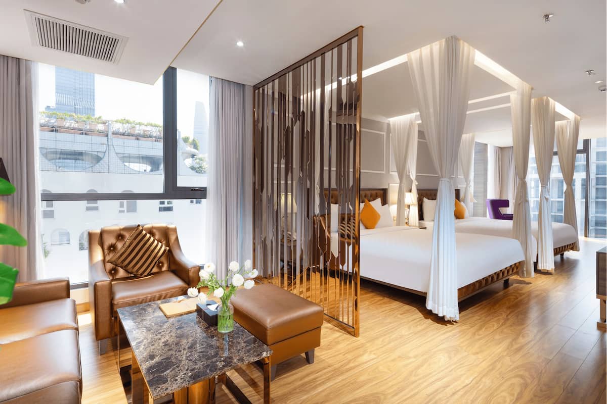 A modern hotel room with a large bed, a sitting area with a table and chairs, and a view of the city through large windows.