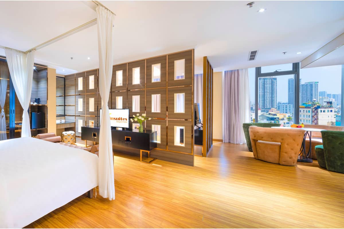 A modern hotel room with a large bed, a desk, a green armchair, and a view of the city.