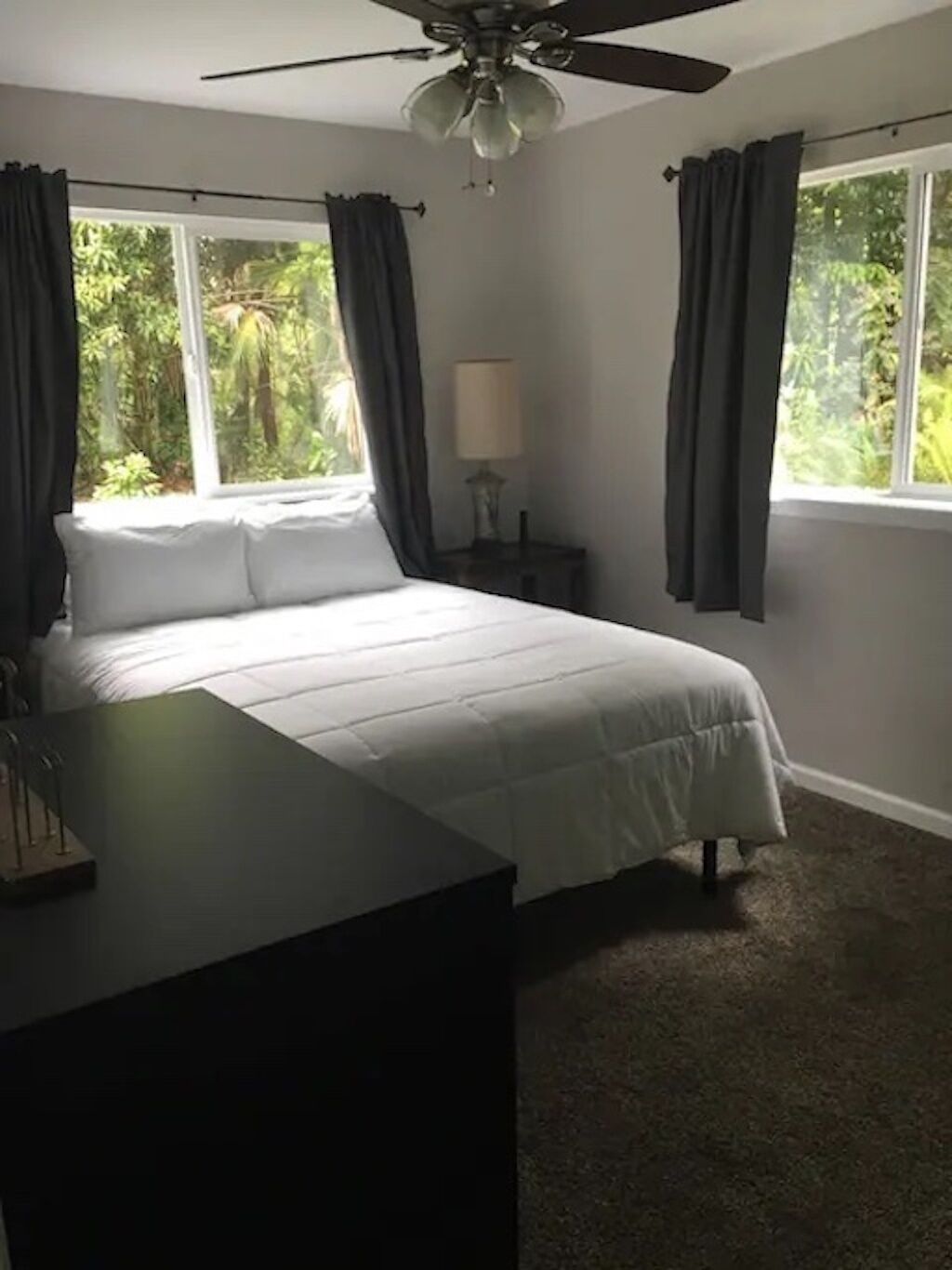 A bedroom with a bed, a desk, a ceiling fan, and a window with curtains.