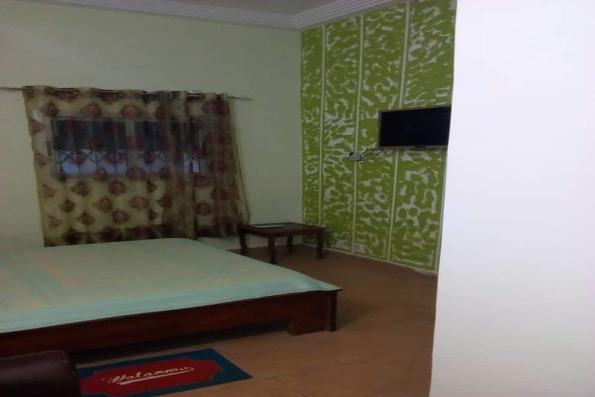 A bedroom with a bed, a small table, a television on the wall, and a patterned wallpaper.