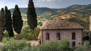 Un bâtiment rustique, doté d’un toit en tuiles, entouré d’oliviers et situé dans un paysage vallonné.