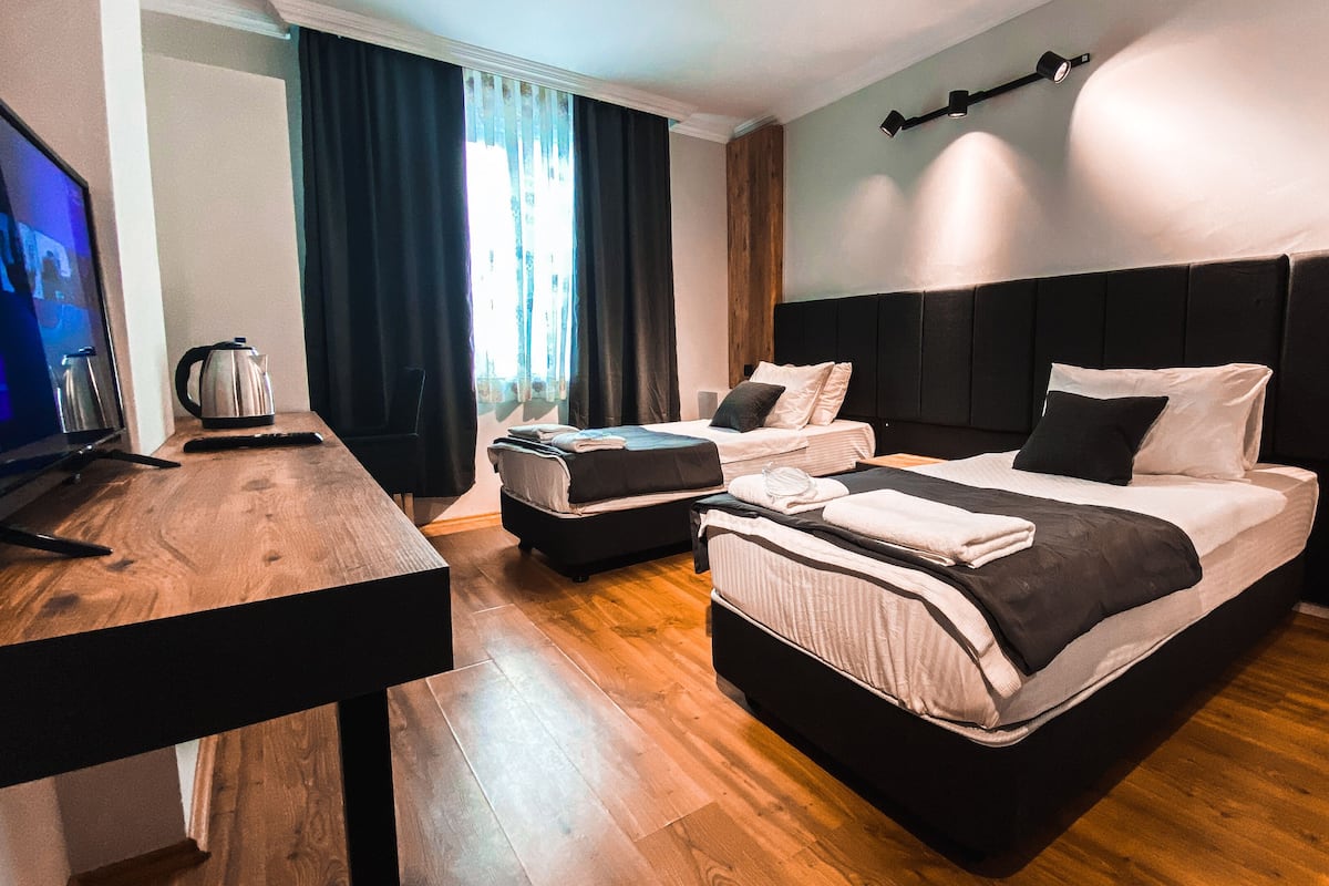 Una habitación de hotel moderna con dos camas, un escritorio de madera, un televisor y un ventanal con cortinas.