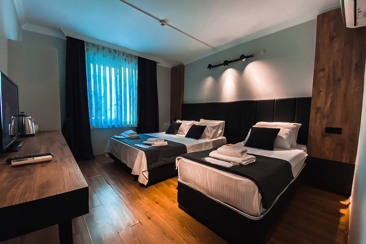 Una habitación de hotel con dos camas, un escritorio, un televisor y una ventana con cortinas.