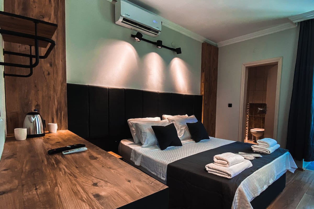 Una habitación de hotel moderna con una cama de madera, una mesita de noche con tetera, tazas y un control remoto.