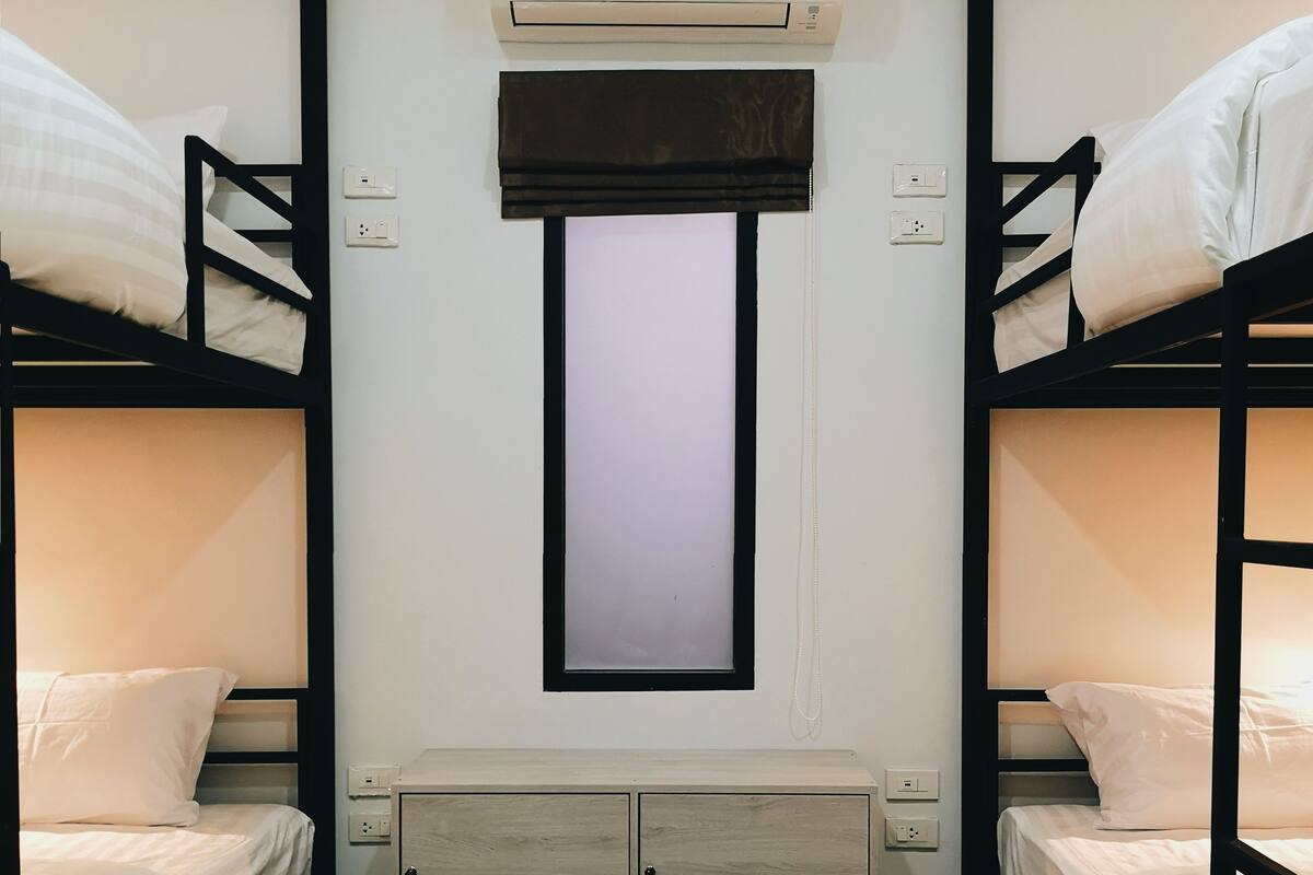 A bunk bed room with a central air conditioning unit, a small window, and a wooden cabinet below the window.