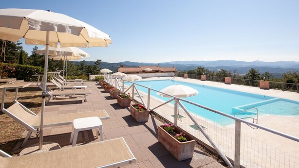 A poolside area with lounge chairs, umbrellas, and potted plants. - Al Castelluccio (Monteverdi Marittimo)