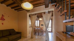 A cozy living room with a sofa, a dining area with a table and chairs, and a staircase with wooden railings. - Al Castelluccio (Monteverdi Marittimo)