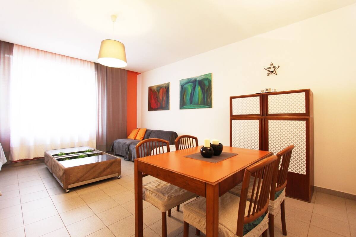 Ein Essbereich mit Holztisch und Stühlen, einer Couch und einem dekorativen Wandbild.