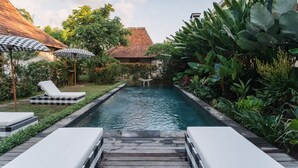 A pool area with lounge chairs and umbrellas, surrounded by lush greenery and a small table. - Relax & rejuvinate at Muda Living, only minutes from Ubud Market! (Ubud)